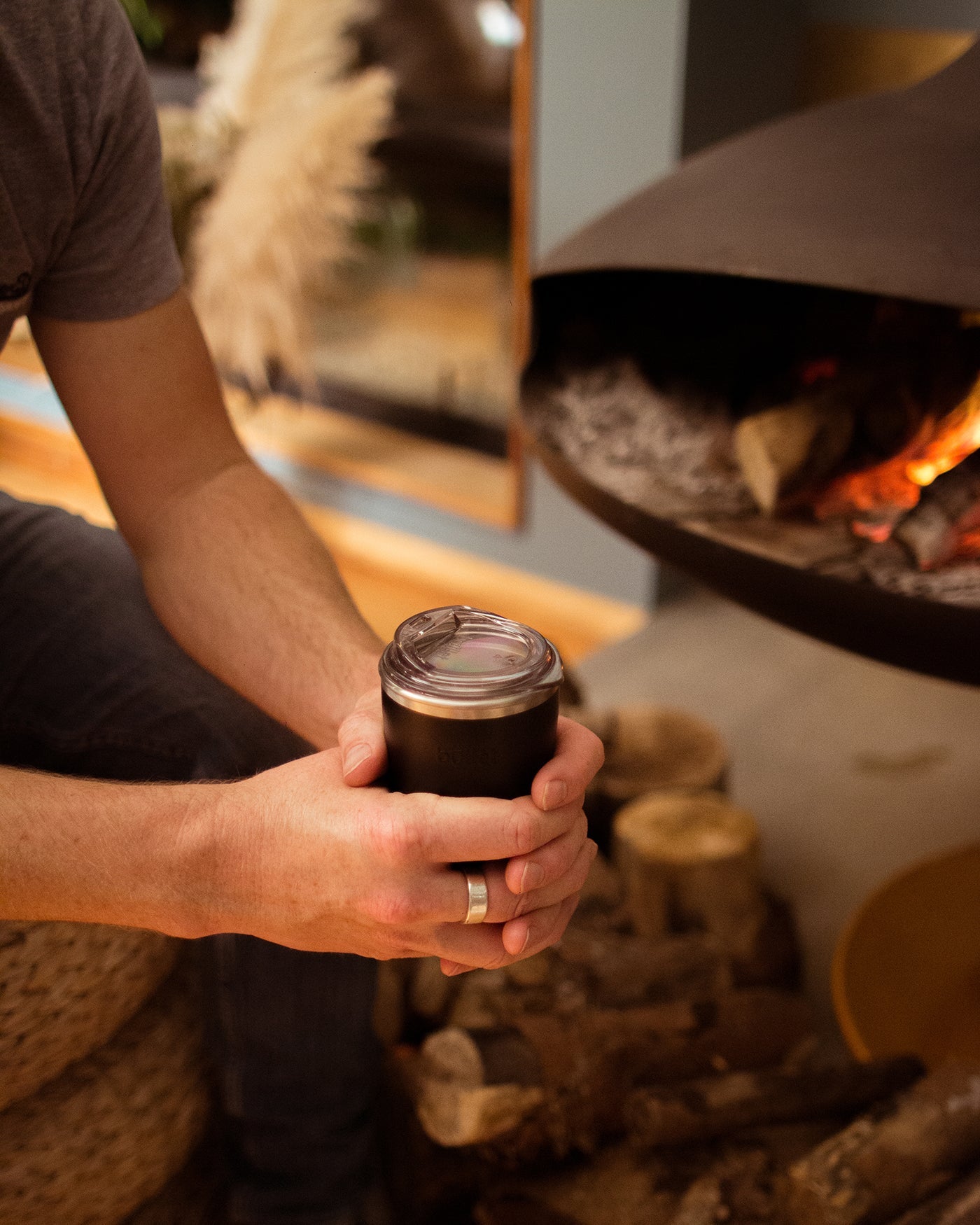 Man embracing a reusable coffee cup next to suspended fire place