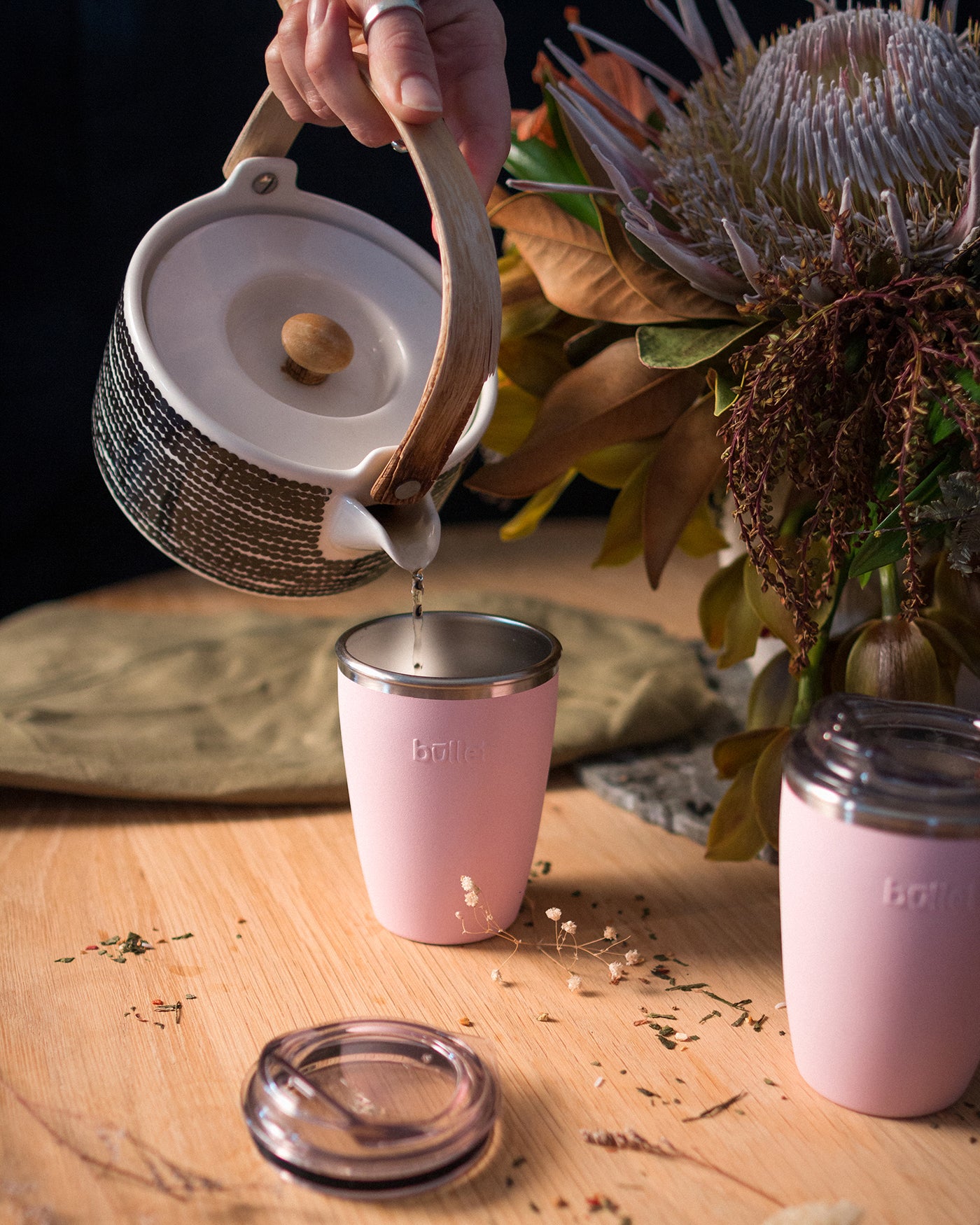 Tea poured into reusable mug amongst flowers on table